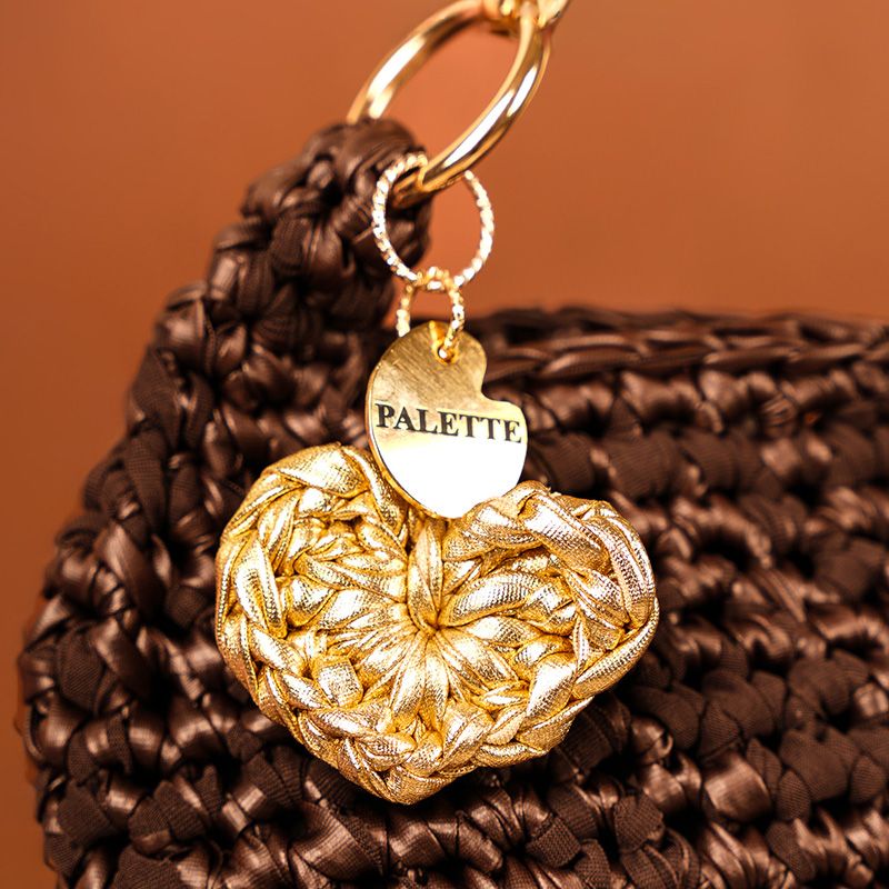 Gold heart-shaped crochet charm with 'PALETTE' branding on a brown hand crafted crochet bag