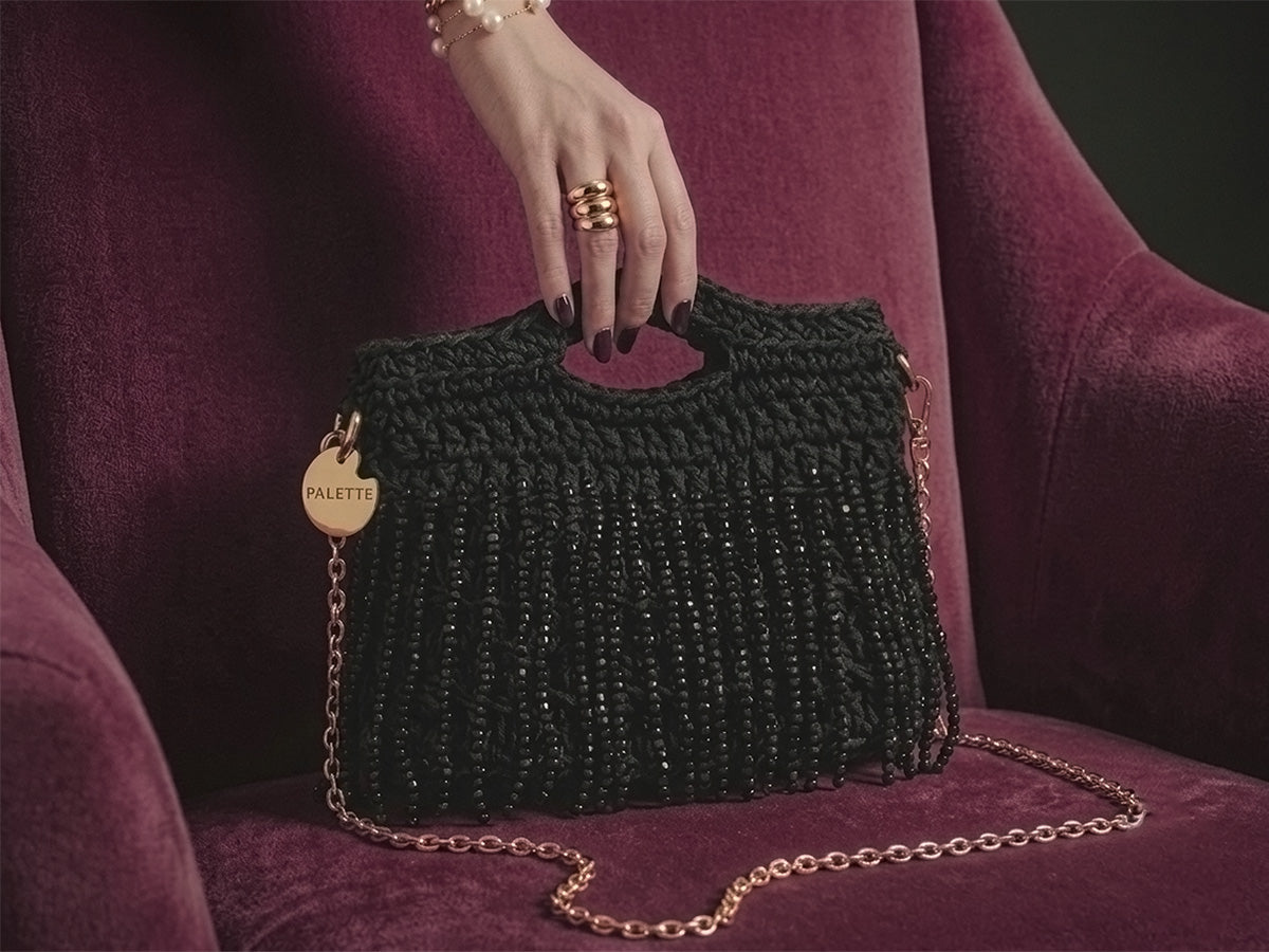 Black beaded handbag from Palette by Rishma with gold chain on a purple chair