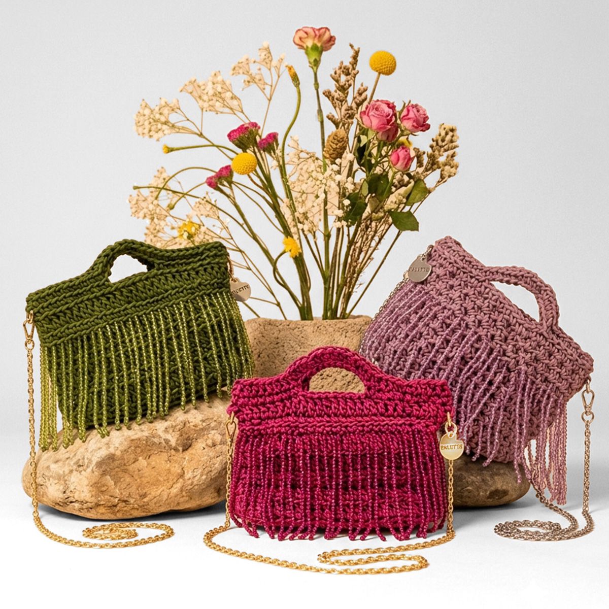 Three crochet handbags in green, red, and pink with beaded fringe tassels with a vase of flowers on a light gray background. -  Palette by Rishma